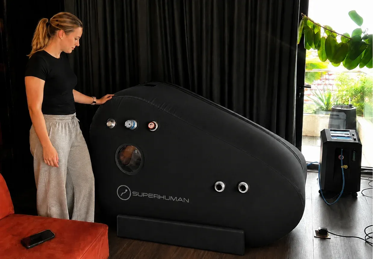 A woman setting up a Superhuman S1 soft-shell hyperbaric chamber at home