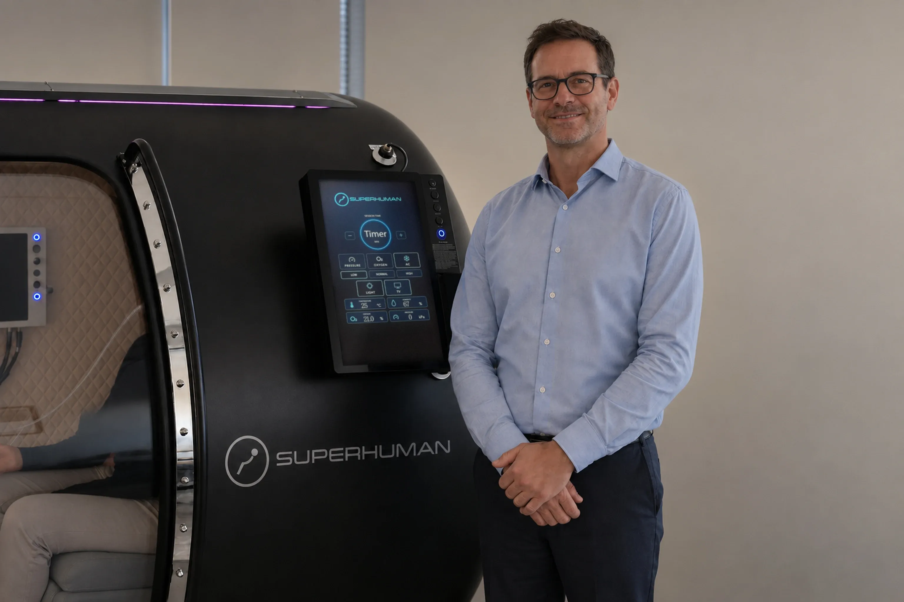 An operator standing beside a Superhuman walk-in chamber, a client seated inside it