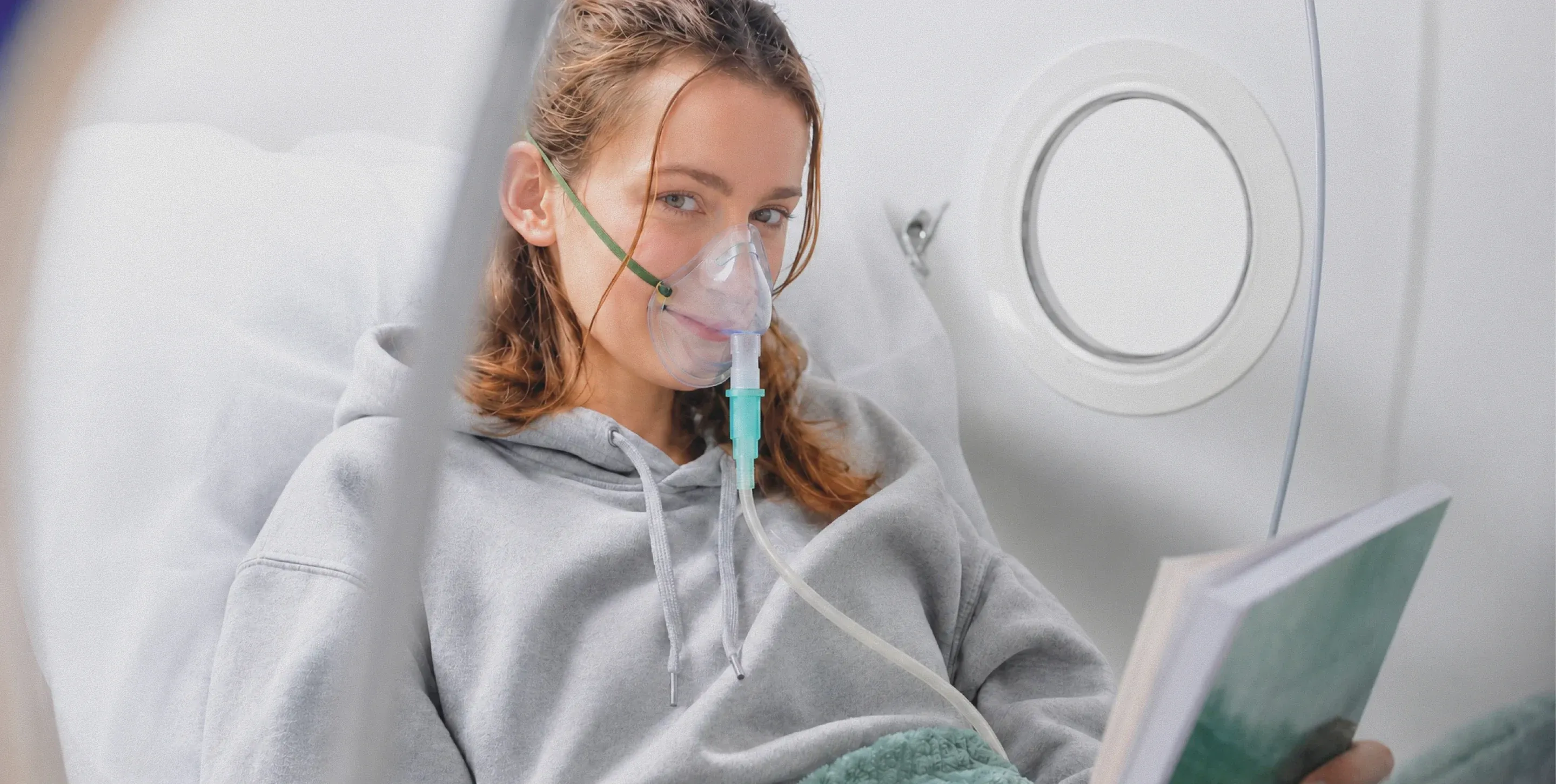 A woman reading a book inside a Superhuman chamber, wearing an oxygen mask