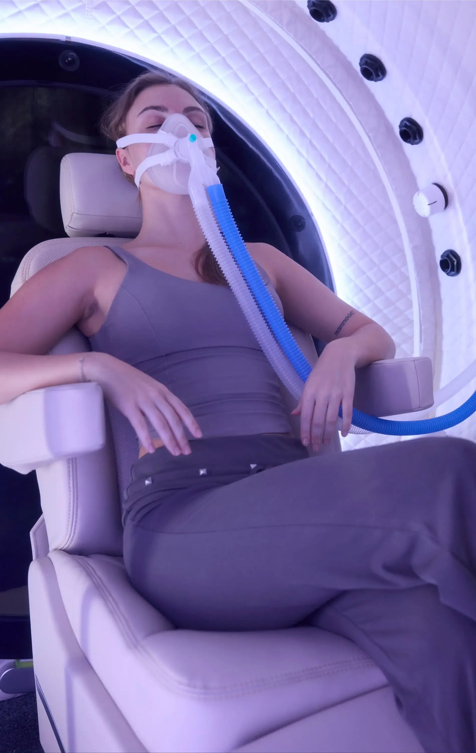 Reclined in the chamber seat with the oxygen mask on and eyes closed