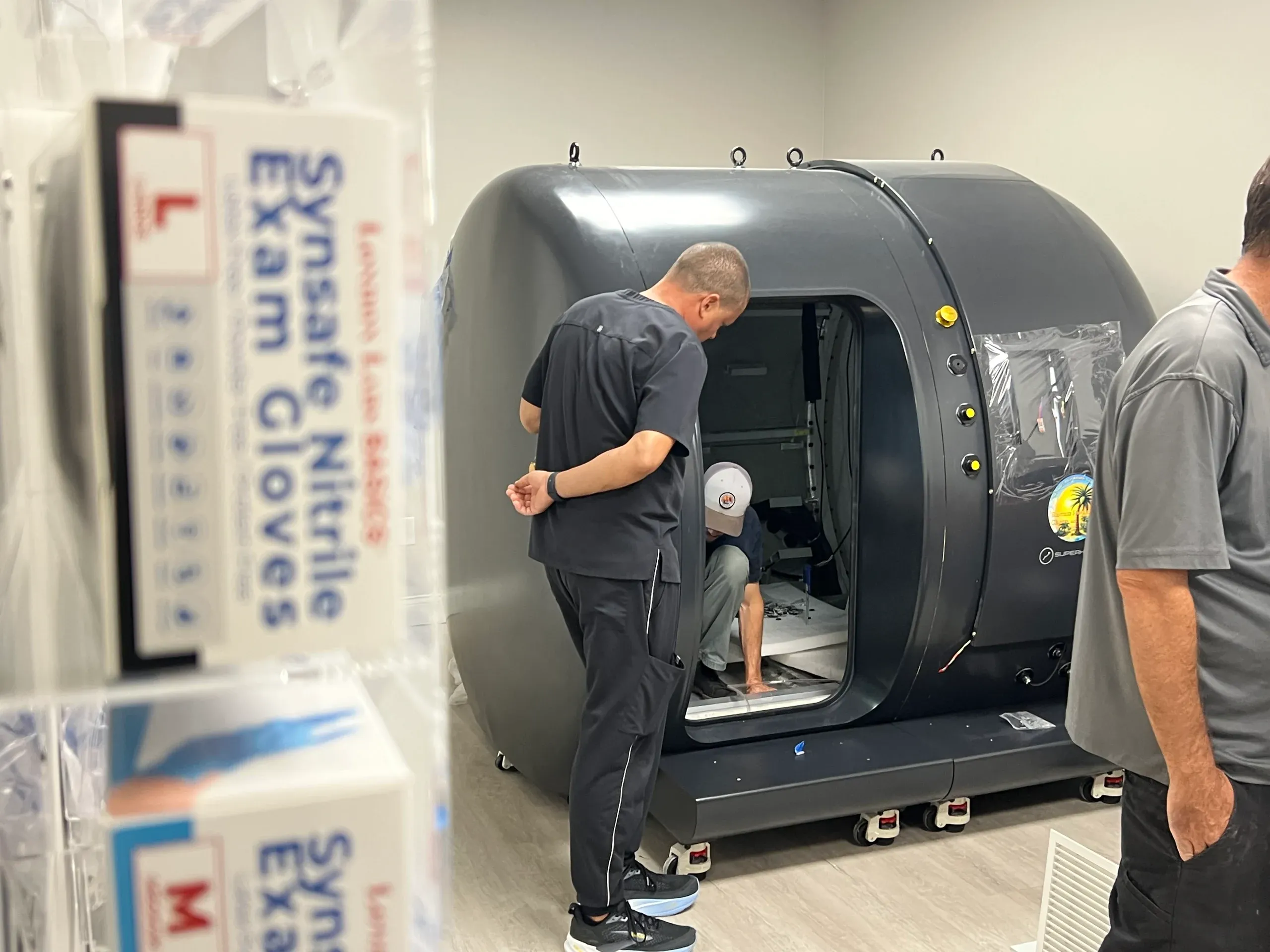 Superhuman installers configuring a walk-in chamber on site while a colleague looks on