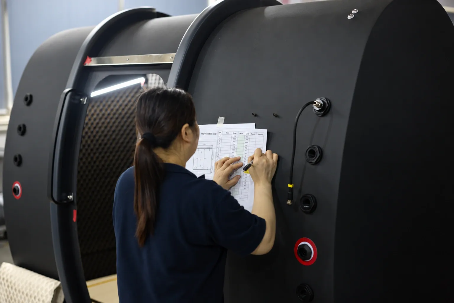 A factory quality-control inspector recording measurements against the build checklist taped to a Superhuman chamber