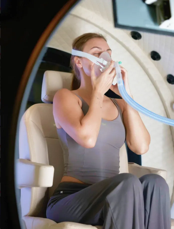 A woman seated in the Superhuman X, holding the oxygen mask to her face