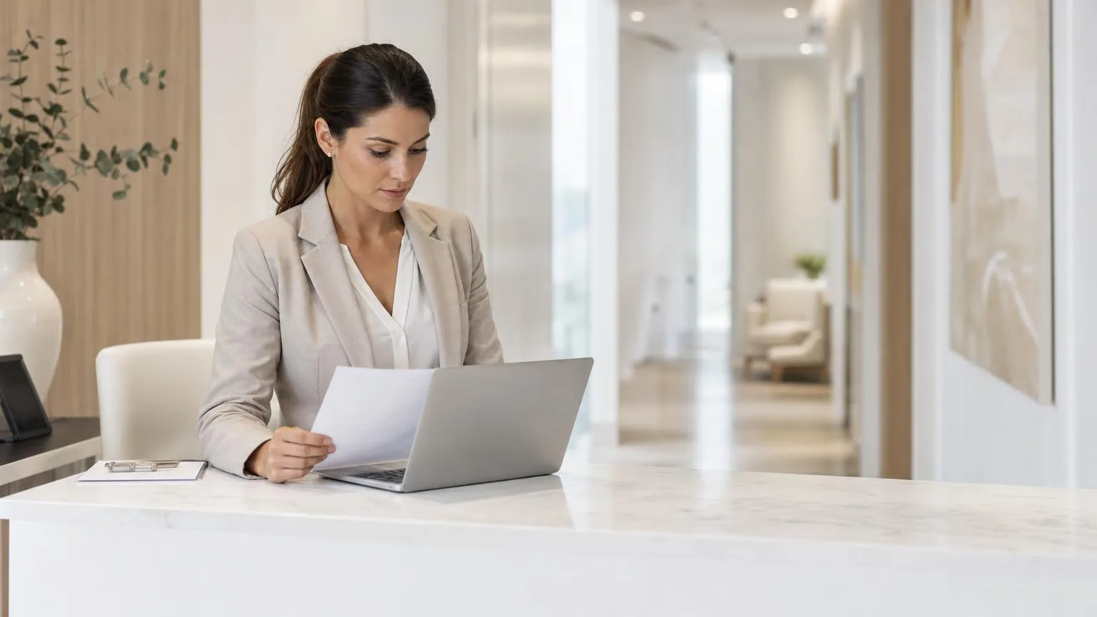 Clinic administrator reviewing billing paperwork next to a laptop at a clean, bright front desk
